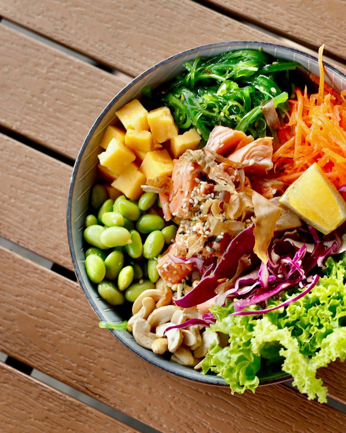 Een pokébowl met rauwe zalmblokjes, komkommer, rode kool en avocado op sushirijst, afgewerkt met sesamzaad en een driehoek nori.